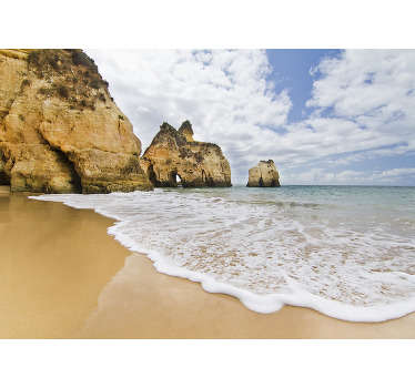 Un diseño de fotomural de paisaje costero que contiene rocas de cuevas alineadas en la misma dirección con el mar inundando la orilla y el cielo azul con nubes.
