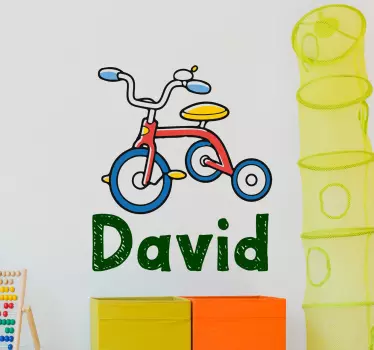 This customisable decorative wall vinyl for children featuring an illustration of a tricycle and the name of your choice underneath